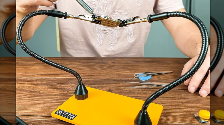 A person using a pair of helping hands to hold a circuit board steady as they solder it.
