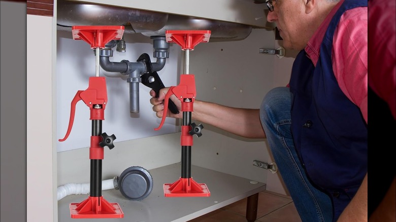 A worker using cabinet jacks under a sink while he works on a plumbing task