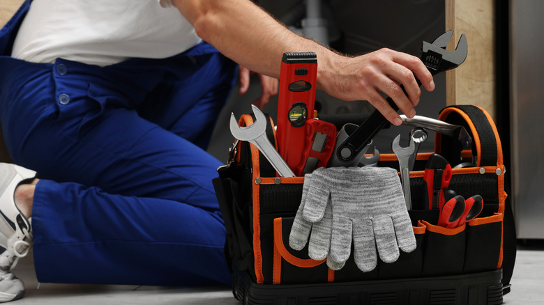 A worker reaching into tool bag and removing an adjustable wrench