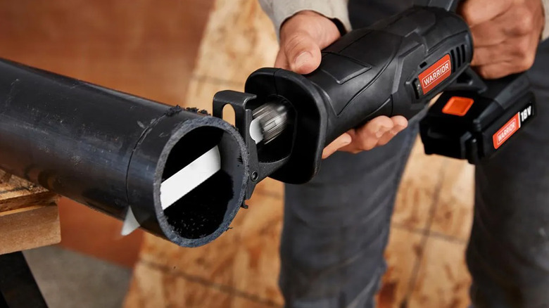 A worker cutting a black pipe with a Warrior reciprocating saw.