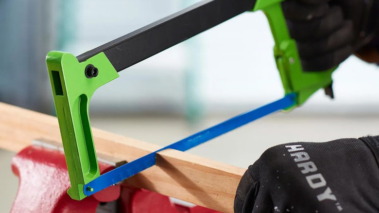 A person cutting a piece of wood with a hacksaw