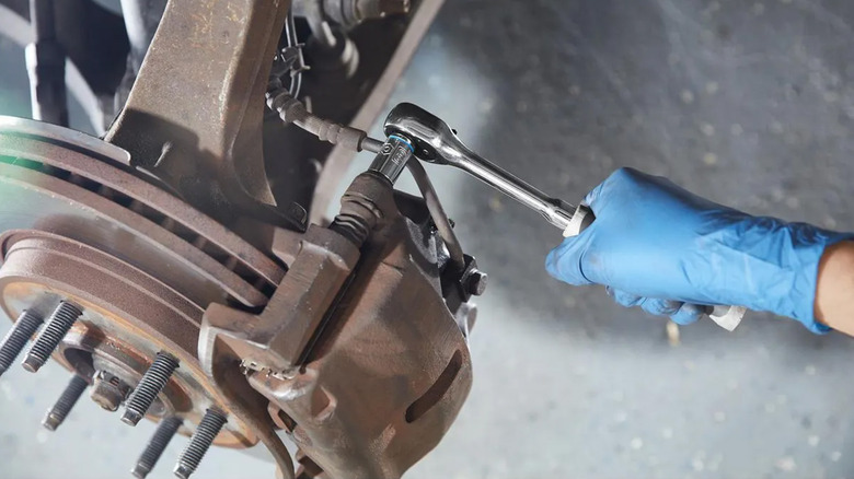 A gloved hand loosening a car's brake system