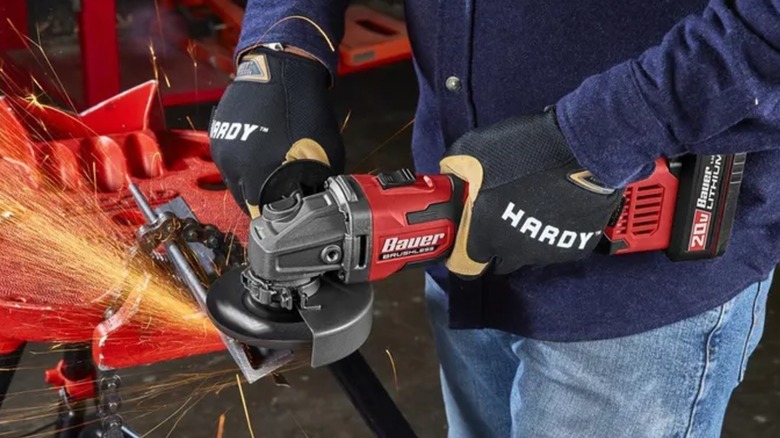 A worker wearing safety gloves shaping metal with Bauer angle grinder