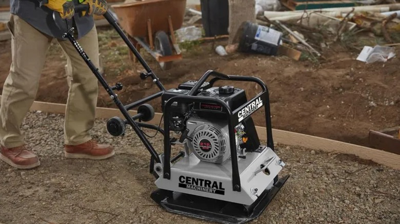 A worker wearing safety gloves using a plate compactor on a job site
