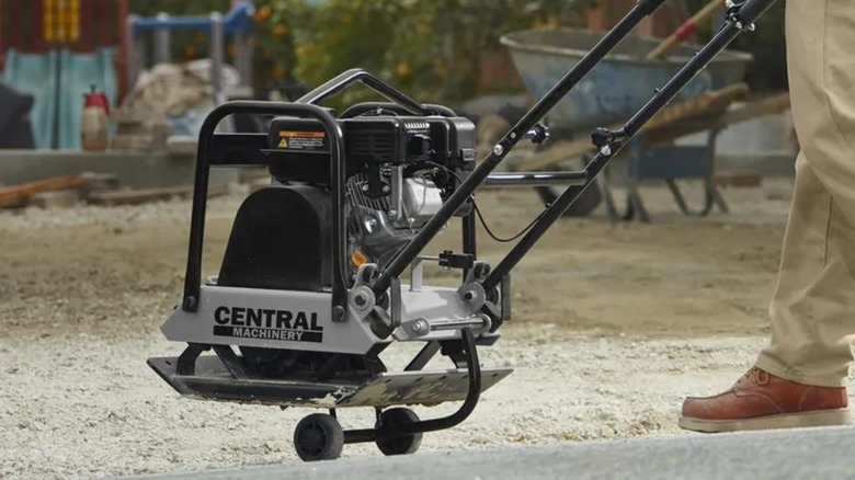 A worker wheeling a Central Machinery plate compactor into position