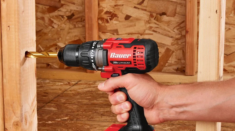 A man using a Bauer compact drill to drill a hole into a two by four
