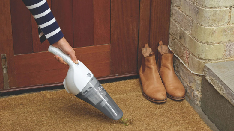 A person vacuuming a carpet with a cordless vacuum.