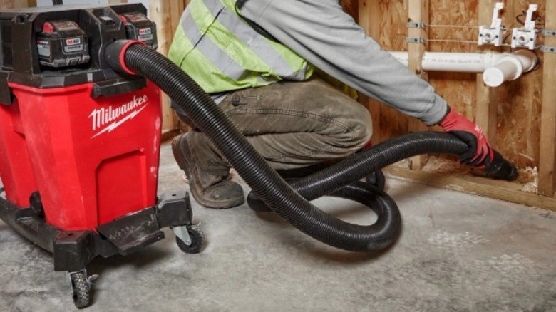 Man using Milwaukee shop vac to remove debris from unfinished wall