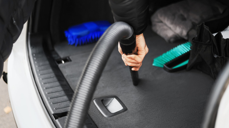 Hand holding vacuum hose to clean a car trunk