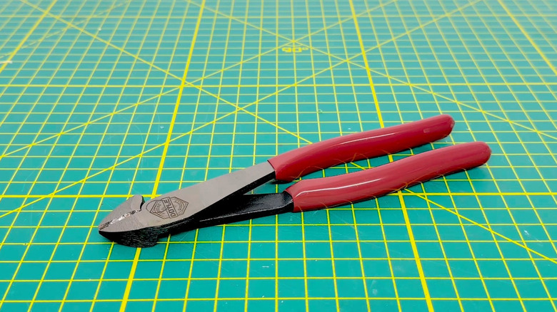 A diagonal cutting plier placed on a green surface with yellow patterns.