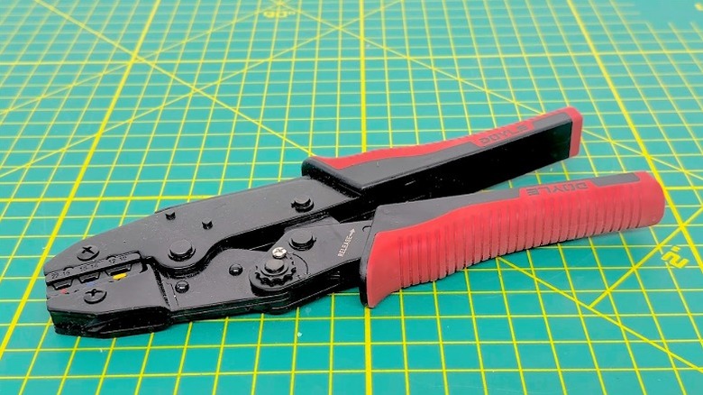 A ratchet crimper placed on a green surface with yellow patterns.