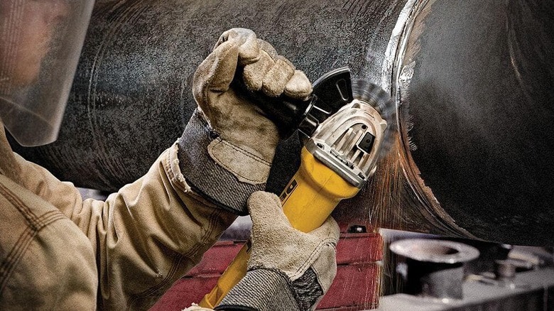 A small angle grinder being used on a big metal pipe.