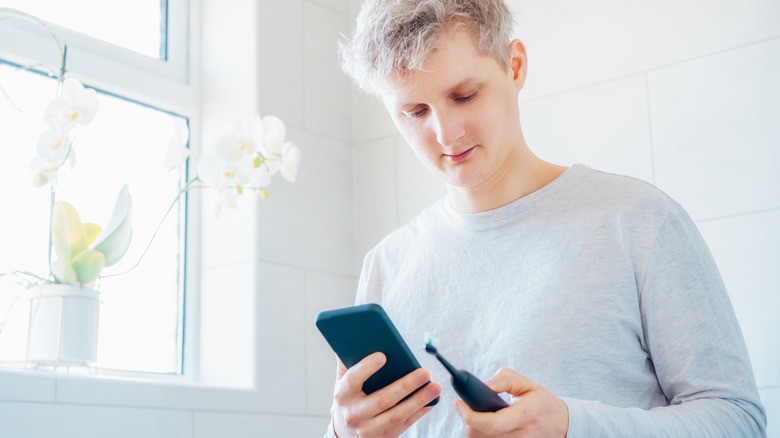 A person holding a toothbrush while looking at a smartphone