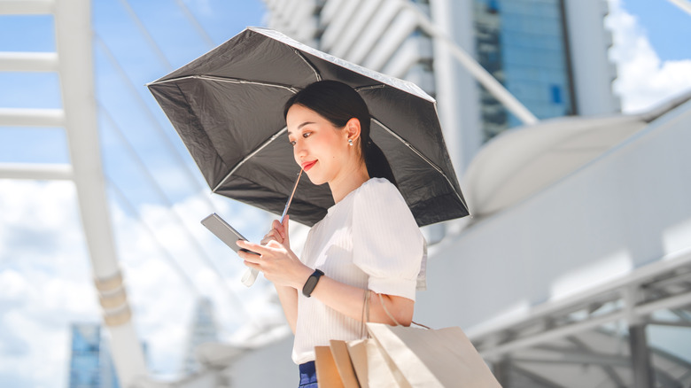 A woman holding a black umbrella and looking at a smartphone