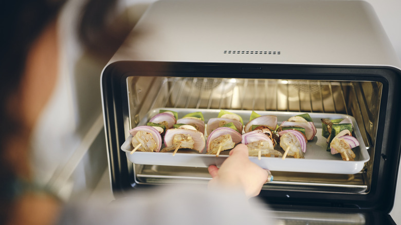 A person pulling a tray of food out of a small oven