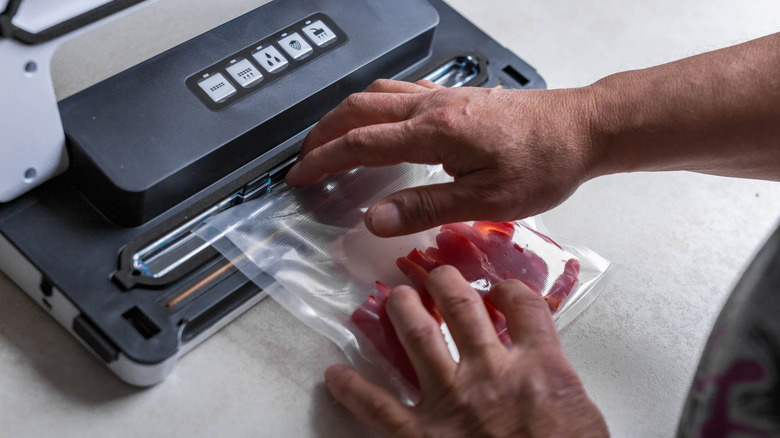 Hands using a vacuum sealing machine on meat