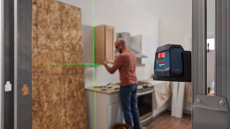 A Bosch cross-line level in the foreground with a man hanging a cabinet in the background.
