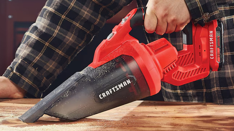 A person cleaning up sawdust with a Craftsman handheld vacuum cleaner.