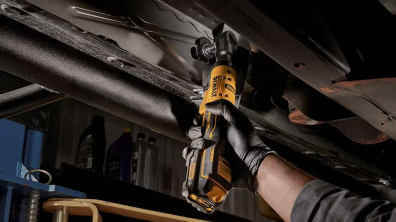 A worker using a DeWalt cordless ratchet on a car.
