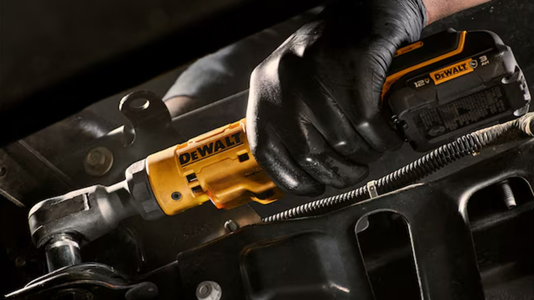 A worker using a DeWalt cordless ratchet on a car.