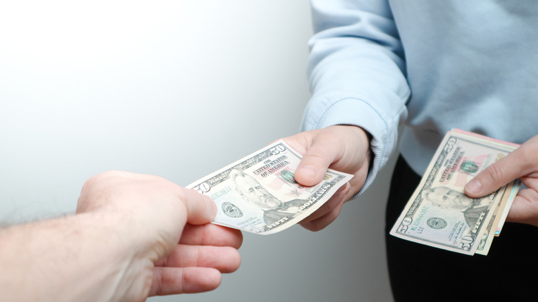 A person giving another person dollar bills