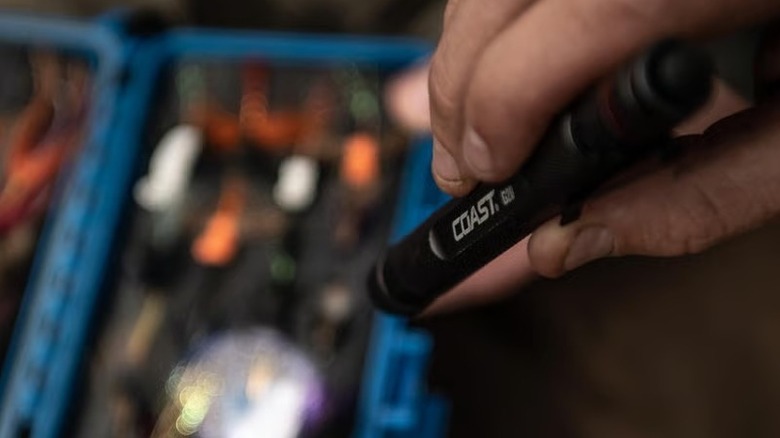A person pointing a Coast LED pen light at a box full of electronic devices