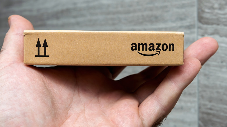 A close-up of a hand holding a small Amazon-branded cardboard box.