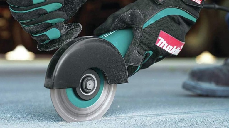 Person using Makita 9557NB Angle Grinder on concrete