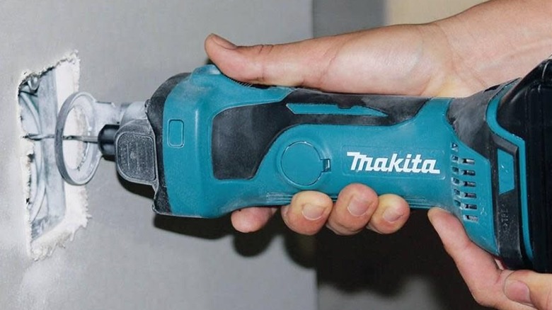 A worker using a Makita XOC01Z cut-out tool to rough-in a power receptacle opening in drywall
