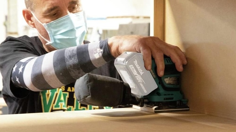 Man using a Makita XOB02Z sander while finishing a piece of wooden furniture