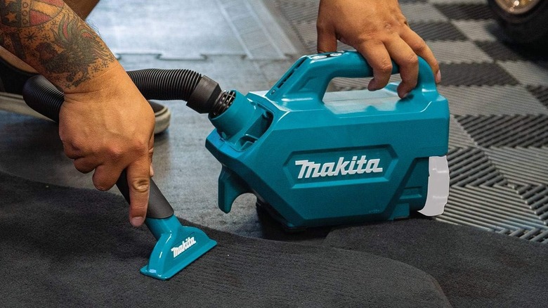 A worker using a Makita XLC07Z to clean a vehicle floor mat