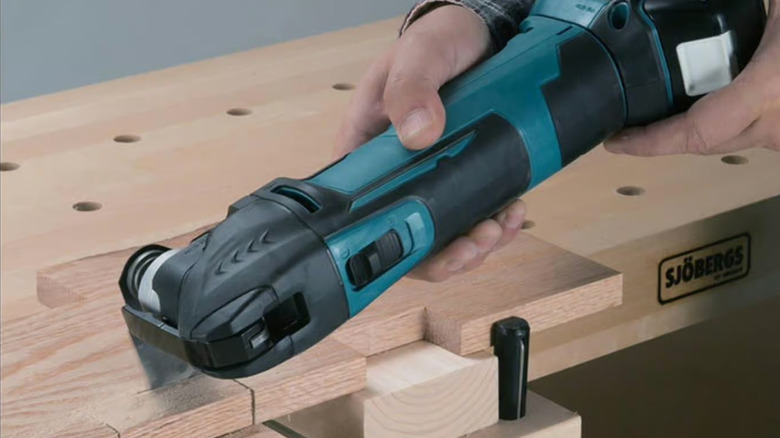 A worker using the Makita XMT03Z multi-tool near a wooden toolbench