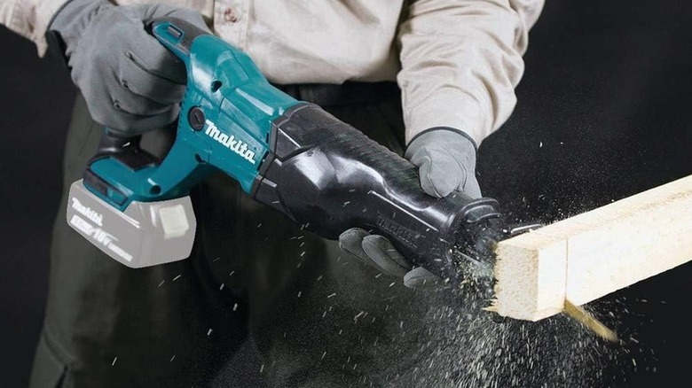 A gloved worker using a Makita XRJ04Z reciprocating saw to cut the end off a 2x4