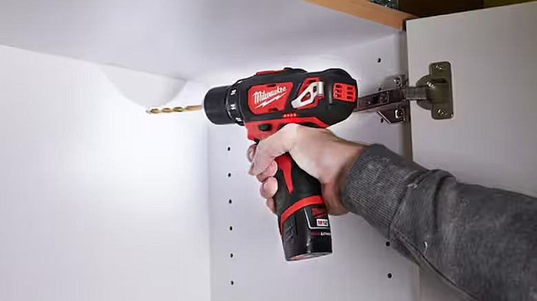 Drilling into a wooden cupboard with a white interior.