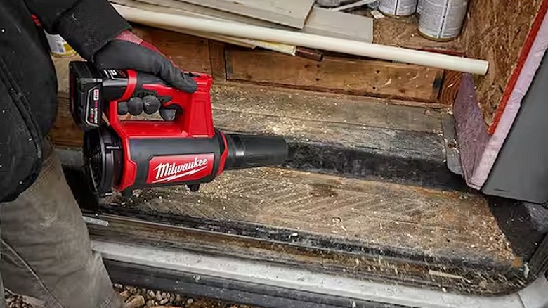 Using a spot blower to clear dust and debris from a wooden surface.