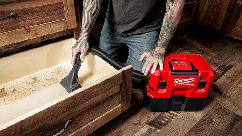 Vacuuming inside a wooden box to clean debris.