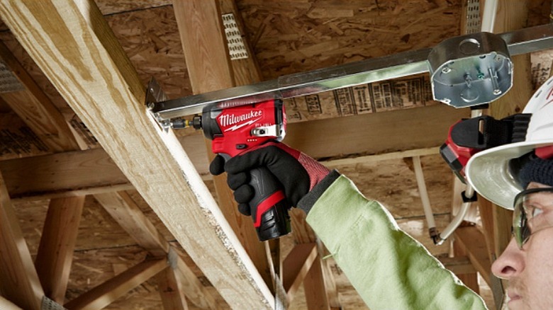 Joining a metal rod to a piece of wood with a fastener using an impact driver.