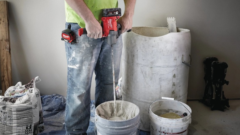 A worker using a Milwaukee mud mixer to mixing paste in a bucket