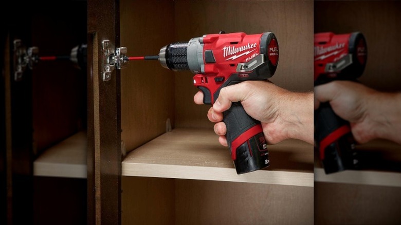 A worker using a Milwaukee drill driver to adjust a cupboard hinge