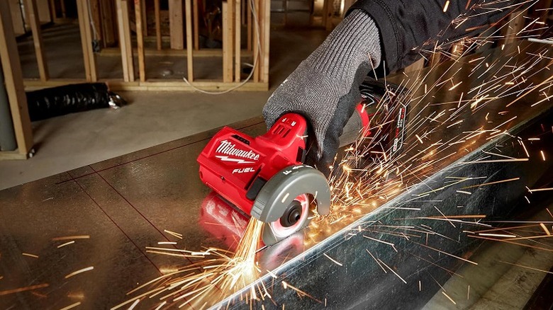 A worker wearing safety gloves using Milwaukee cut off tool to trim a piece of metal