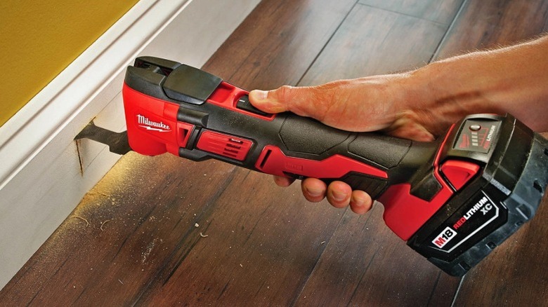 A worker using a Milwaukee multi-tool to cut wall molding trim