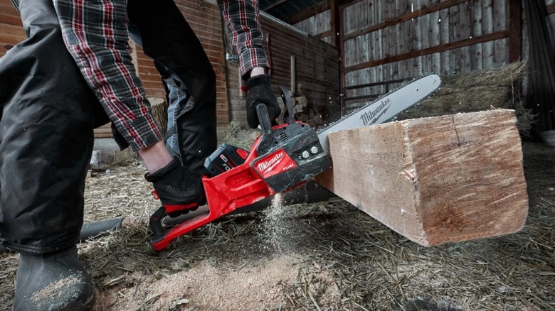 A worker wearing safety gloves cutting a piece of lumber with a Milwaukee chainsaw