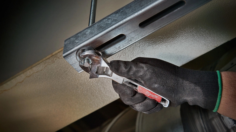 A gloved hand using a Milwaukee Adjustable Wrench.