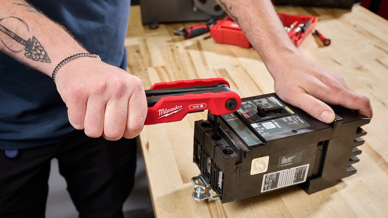 A person using the Milwaukee Electrician's SAE Folding Hex Key Set on a battery.