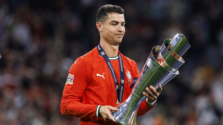 Ronaldo wearing the red Portugal jersey, holding the Nations League trophy with a medal around his neck.