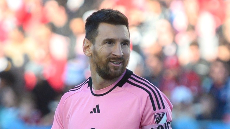 Lionel Messi wearing the pink Inter Miami jersey, standing on the pitch and smiling.