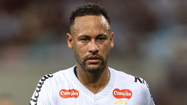 Neymar walking on the pitch during a match, wearing a white Santos F.C. jersey.