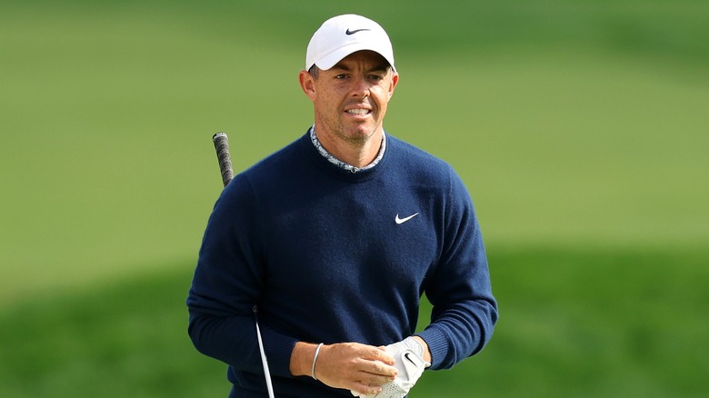 Rory wearing a Nike blue cardigan and white cap, holding a golf club and golf gloves.