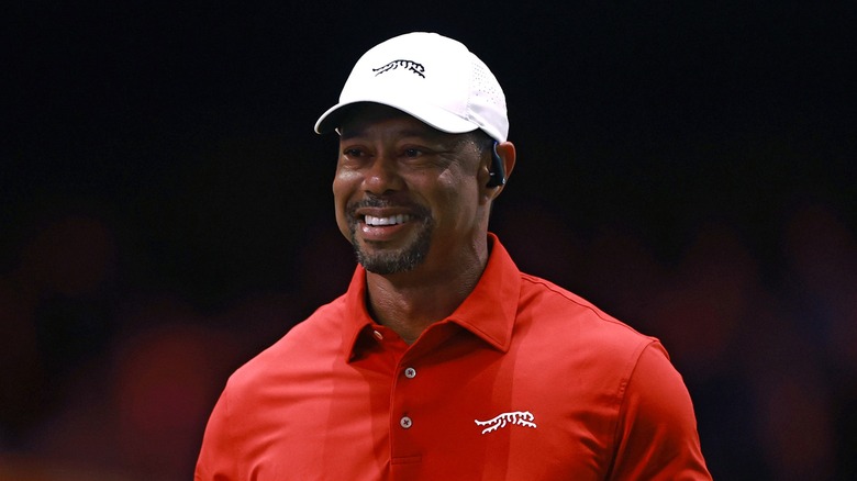 Tiger Woods wearing a Sun Day Red white cap and red shirt, smiling with a communication earpiece on.