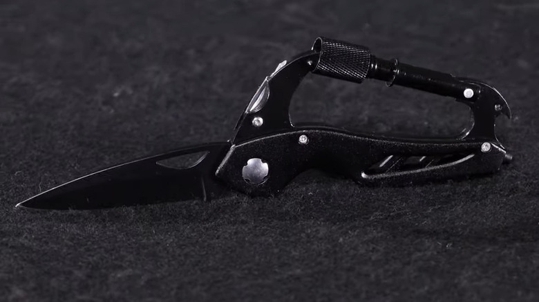 Black carabiner multitool on black carpet with black knife extended